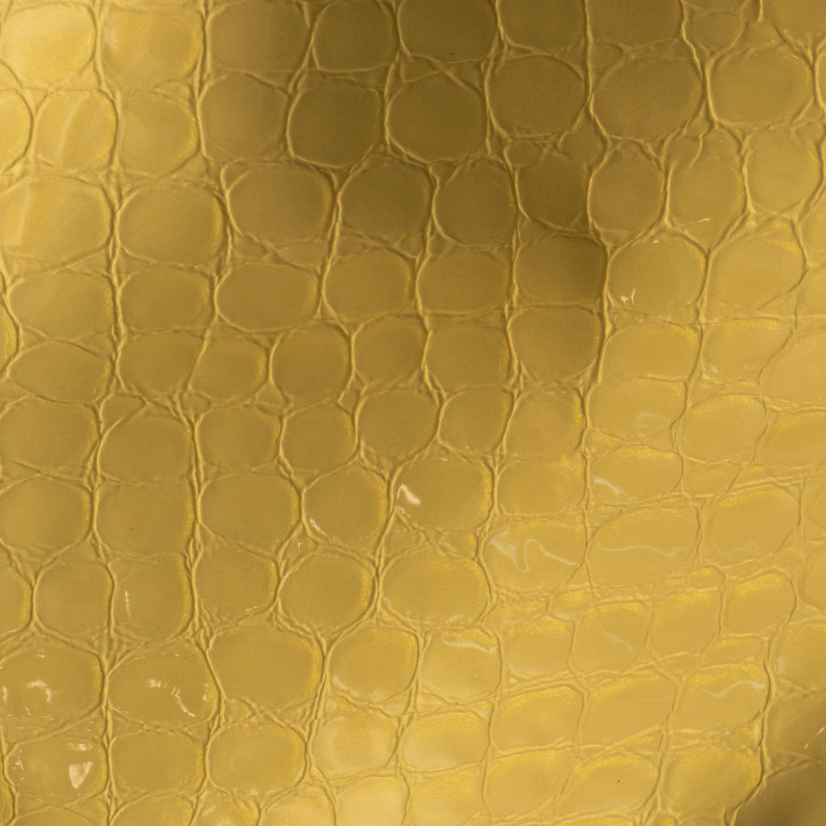 A close-up of a textured gold leather material with a raised reptile or crocodile pattern and a soft gradient sheen.