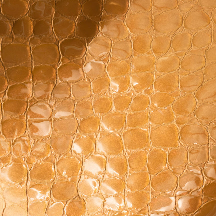 A close-up of glossy, textured material with a repeating rounded scale pattern in warm metallic copper, bronze, and gold tones.