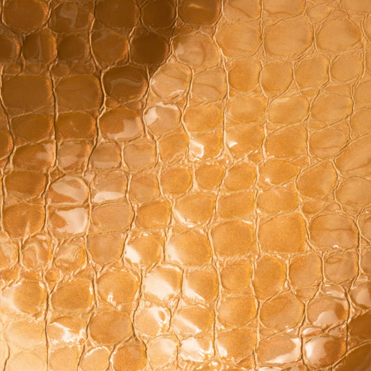 A close-up of glossy, textured material with a repeating rounded scale pattern in warm metallic copper, bronze, and gold tones.