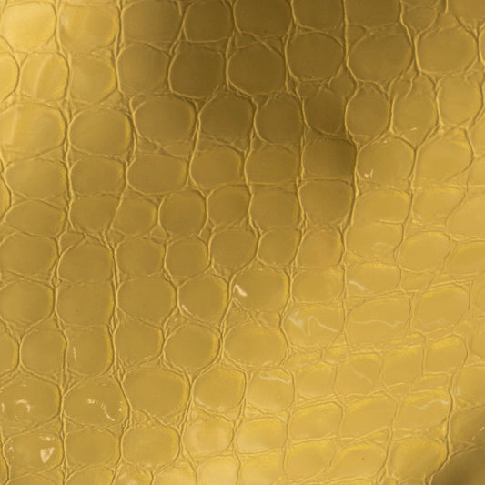 A close-up of a textured gold leather material with a raised reptile or crocodile pattern and a soft gradient sheen.