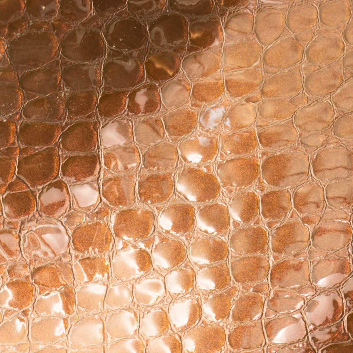 A close-up of a textured material with a glossy, pebbled or reptile-scale pattern in warm coppery brown and bronze tones.