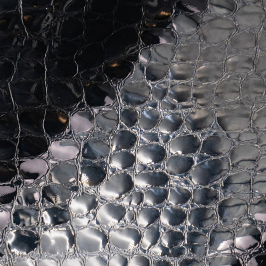 Close-up of a glossy black textured material with a raised reptile or alligator-scale pattern and reflective highlights.